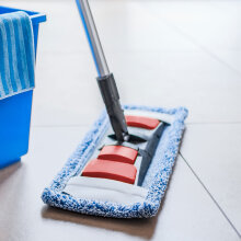 Ein Teleskopstiel mit einem blauen Wischmopp steht neben einem blauen Putzeimer mit Microfasertuch.