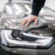 Eine Hand wischt mit einem grauen Auto-Poliertuch über den Scheinwerfer eines Autos.
