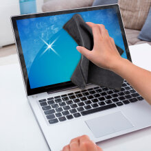 Eine Person reinigt den Bildschirm eines Laptops mit einem grauen Soft Microfasertuch.