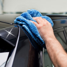 Hand wischt mit einem blauen Auto-Poliertuch die...
