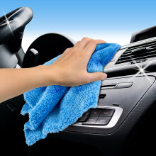 Hand wischt mit einem blauen Autotuch über das Armaturenbrett und die Lüftungsschlitze eines Autos.