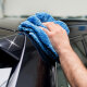 Hand wischt mit einem blauen Auto-Poliertuch die Karosserie eines schwarzen Autos.