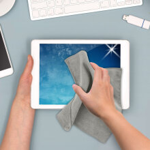 Hand wischt mit einem grauen Microfasertuch über den Bildschirm eines Tablets auf einem Schreibtisch.