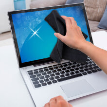 Hand wischt mit einem schwarzen Soft-Microfasertuch über den Bildschirm eines Laptops.