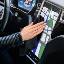 Hand wischt mit einem schwarzen Soft-Microfasertuch über den Touchscreen eines Autos.